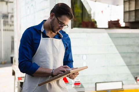 Artisan vendor managing orders on tablet beside food truck