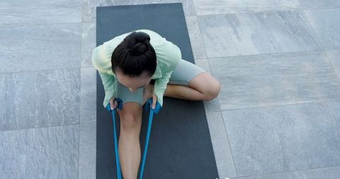 Woman stretching with resistance band on outdoor mat for fitness