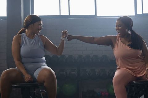 African american women celebrating post-workout fist bump in backlit gym