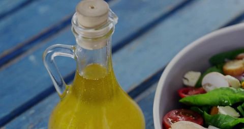 Corked glass oil cruet with rustic vegetable salad on blue table