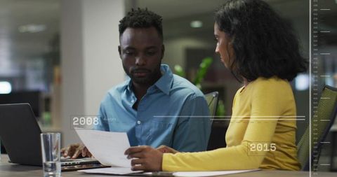 Professionals reviewing documents and collaborating on laptop in modern office workspace