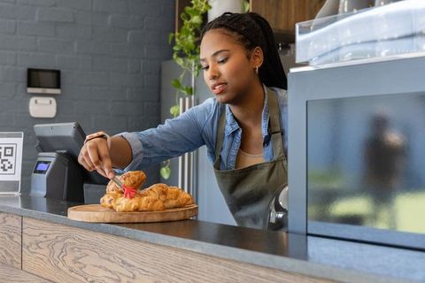 African american barista arranging fresh croissants on wooden board at modern cafe counter