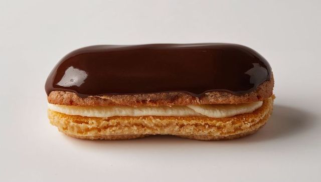 Chocolate-glazed éclair resting on white surface showing cream filling and crumbly choux