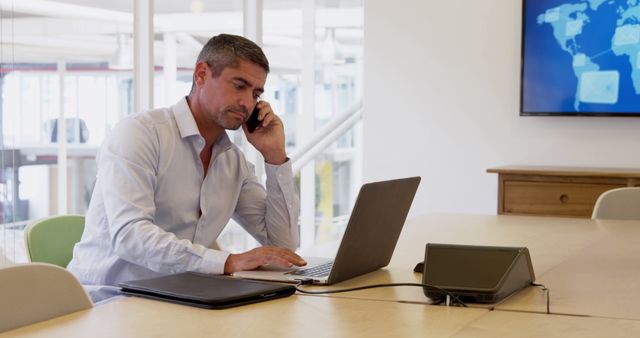 Businessman Working on Laptop While Talking on Phone in Modern Office - Download Free Stock Images Pikwizard.com