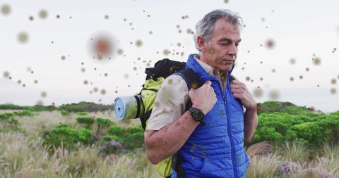 Middle-aged hiker pausing on coastal scrub carrying backpack with foam pad in reflective solitude