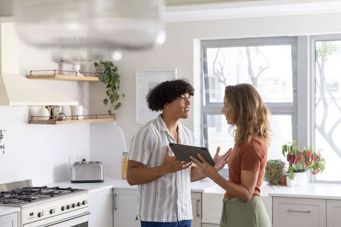 Couple discussing while holding tablet in modern sunlit kitchen, deciding together