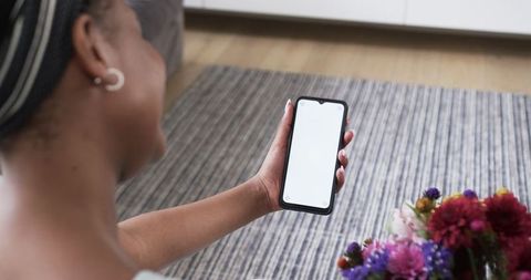 Young woman holding smartphone with blank screen indoors