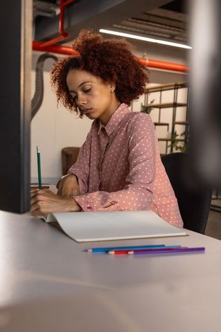 Focused woman writing in creative office with colored pencils