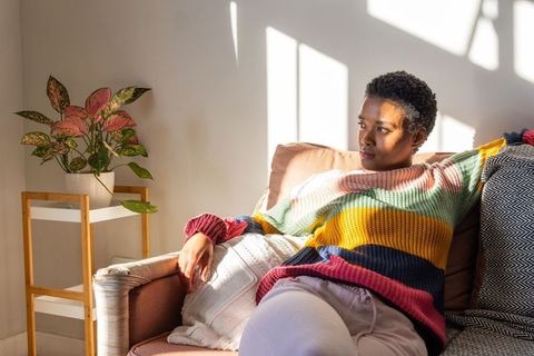Sunlit african american woman relaxing on sofa in colorful chunky knit sweater, cozy home
