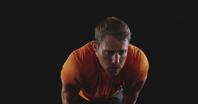 Focused Man in Orange Shirt Exercising Against Black Background - Download Free Stock Images Pikwizard.com
