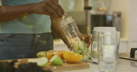 Woman preparing fruit smoothie in blender cup on kitchen countertop for healthy living