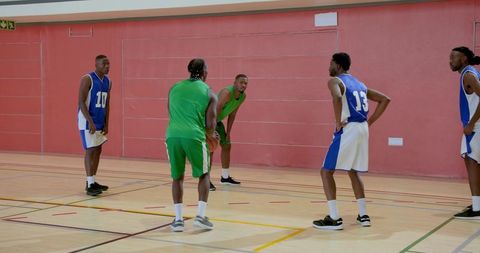 Basketball players dribbling and defending during indoor practice drill on hardwood court