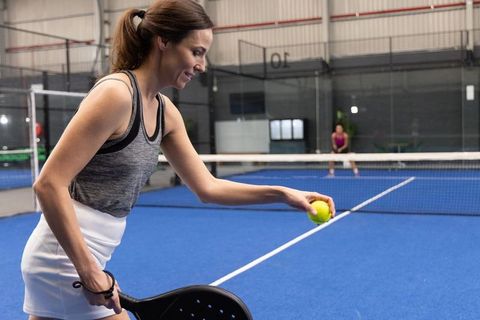 Female player serving on indoor padel court blue surface preparing volley with paddle