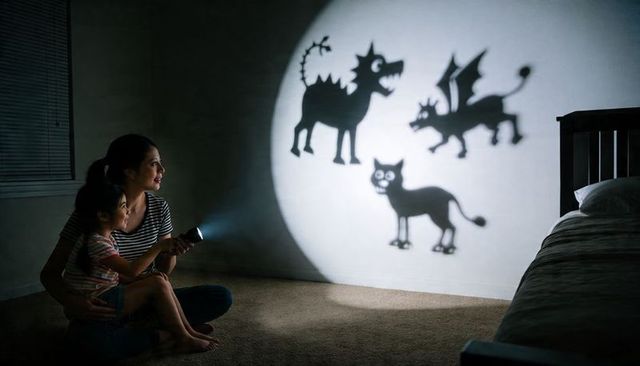 Mother and daughter casting playful monster shadows on bedroom wall with flashlight