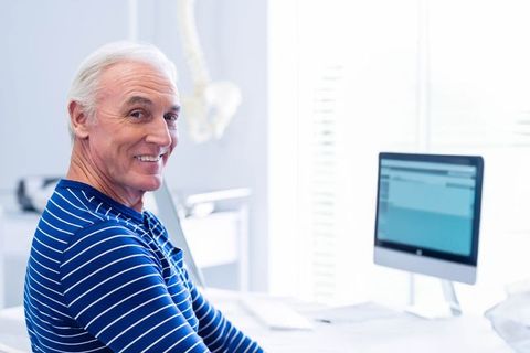 Senior Healthcare Professional Smiling at Desk with Computer and Spine Model