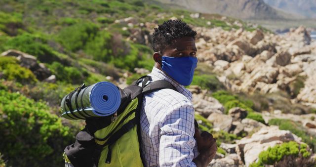 African american man wearing face mask exercising outdoors hiking in countryside on a mountain. Fitness training and healthy outdoor lifestyle during coronavirus covid 19 pandemic.