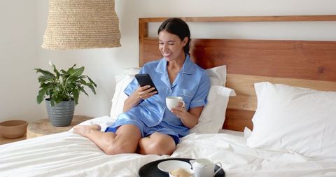 Woman in Blue Satin Pajamas Using Smartphone on Bed