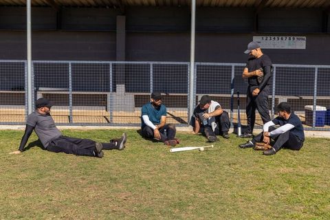 Baseball teammates sitting and relaxing by dugout between practice drills on sunny field