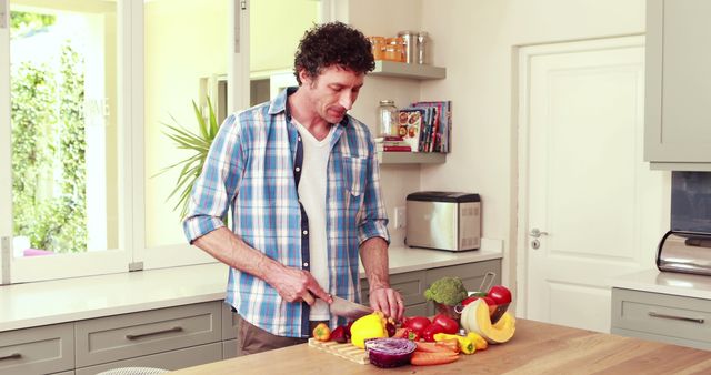 Man cutting bell pepper and various vegetables on countertop in modern kitchen. Perfect for content on healthy lifestyles, home cooking, or kitchen appliances. Ideal for blogs, culinary magazines, healthy eating campaigns, and recipe websites.