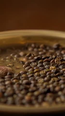 Vertical video bobbing roasted coffee beans floating in amber liquid revealing pink husk