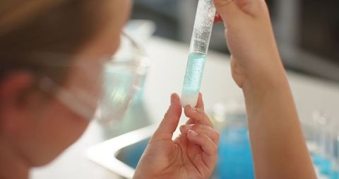 Female teenager examining test tube with blue-green solution during science experiment