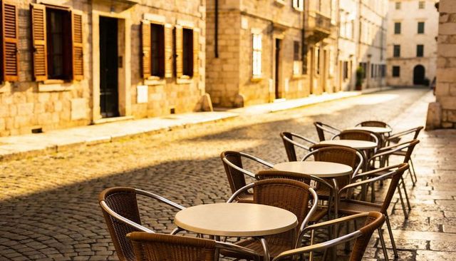 Sunlit european cobblestone cafe terrace basking in golden hour light with wicker chairs