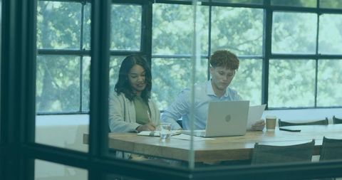 Collaborating professionals reviewing documents at glass-walled office table