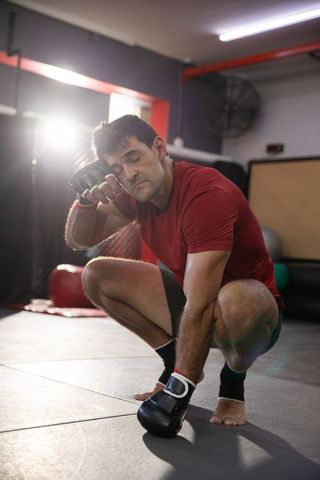 Exhausted mixed martial artist squatting and catching breath in cage gym