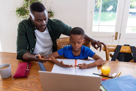 African american father helping son with math homework at home using laptop