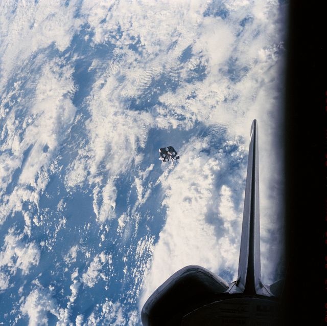Foot restraint floating near Space Shuttle Challenger during February 9, 1984 extravehicular activity session led by astronauts Bruce McCandless II and Robert Stewart. Blue Earth backdrop and atmosphere visible. Ideal for education on space missions, NASA operations, or space debris management.