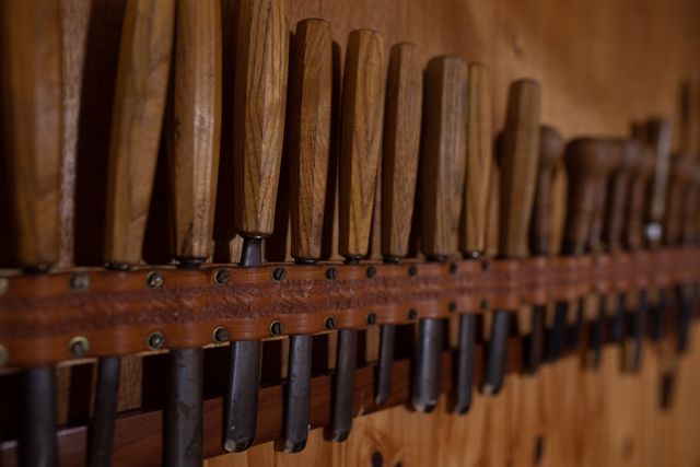 Close up view of a row of chisels belonging to a luthier in a workshop, part of the tools of their trade, hanging on the wall.