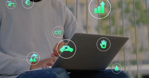 Worker typing on laptop with green sustainability icons overlay, eco productivity concept