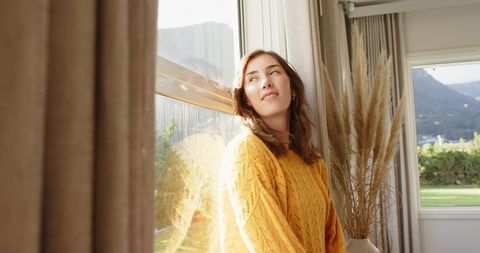 Sunlit Cozy Morning: Woman Relaxing by Window in Mustard Sweater with Pampas Grass