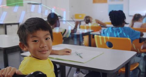 Smiling schoolchild writing in notebook at classroom desk with pencil and yellow shirt