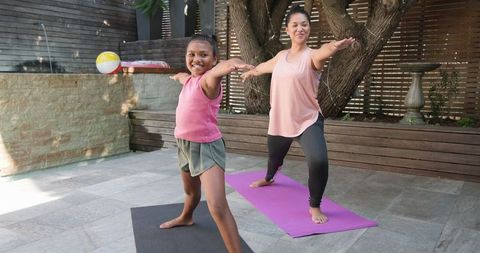 Mother and daughter practicing yoga outdoors with backyard serenity