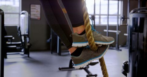 Caucasian woman climbing rope in modern fitness studio