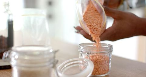 Person Organizing Pantry by Storing Red Lentils in Glass Jar