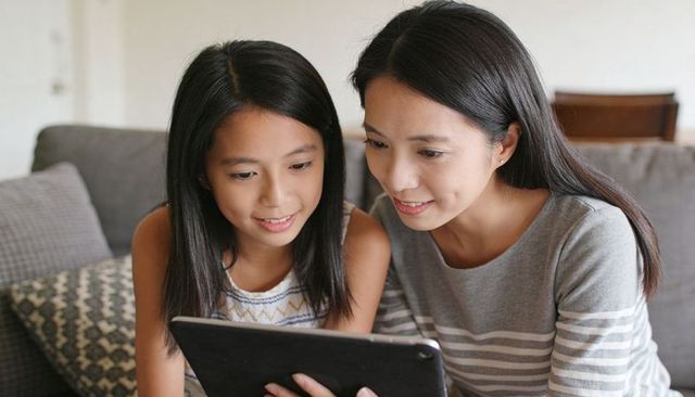 Mother and daughter bonding while using tablet on sofa at home, family technology