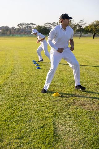 Cricket players practicing footwork agility drill on grass with cones