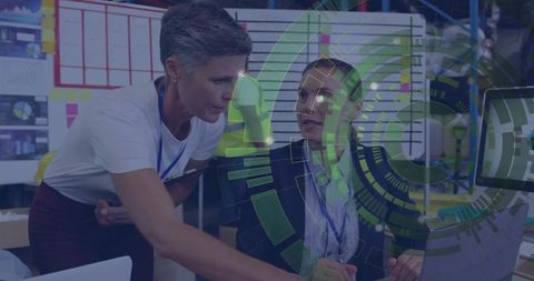 Mature manager leaning and pointing at laptop while collaborating with colleague in warehouse HUD