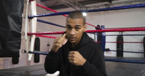 Intense boxer training in ring wearing hoodie punching and wiping sweat with towel