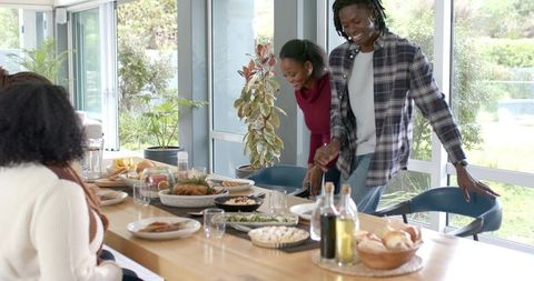 Sunlit family-style gathering featuring diverse friends placing roast and bread at table