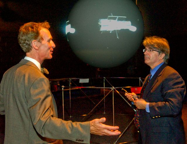 Bill Nye and Dr. Jim Garvin are seen discussing something next to the Science on a Sphere exhibit at NASA's Goddard Space Flight Center during a tour on September 8, 2011. The image shows them in a professional, yet engaging conversation, making it ideal for use in educational content related to space exploration, scientific events, or NASA's missions. This also could be utilized by educational websites, science blogs, and articles highlighting collaboration between prominent science communicators and NASA scientists.