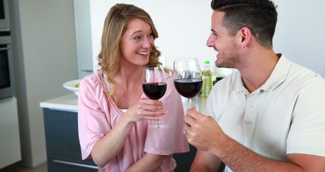 Couple sharing a cheerful moment while drinking red wine. Perfect for representing love, togetherness, relaxation, and enjoying simple pleasures. Ideal for use in marketing campaigns related to food and wine, lifestyle blogs, and social media posts centered on relationships and happiness.