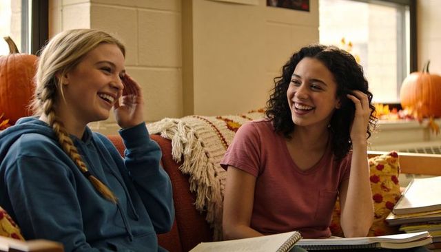 Laughing students studying on cozy autumn lounge couch with pumpkins and notebooks