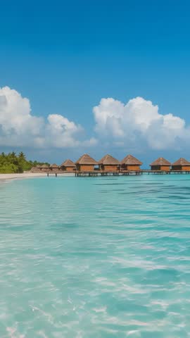 Vertical video panning turquoise lagoon toward overwater bungalows and palm beach