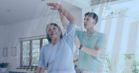 Caregiver guiding senior woman through arm exercise in sunlit living room