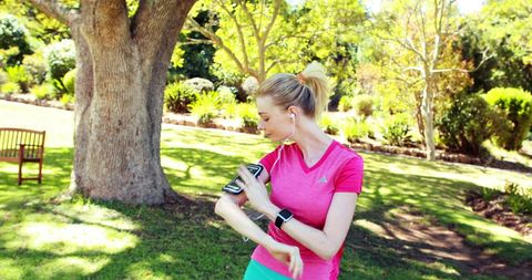 Fit young woman exercising with fitness tracker in sunny park
