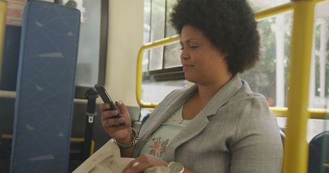 Woman with afro hairstyle smiling while using smartphone on bus