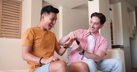 Happy Diverse Male Couple Connecting Joyfully at Home with Smartphone